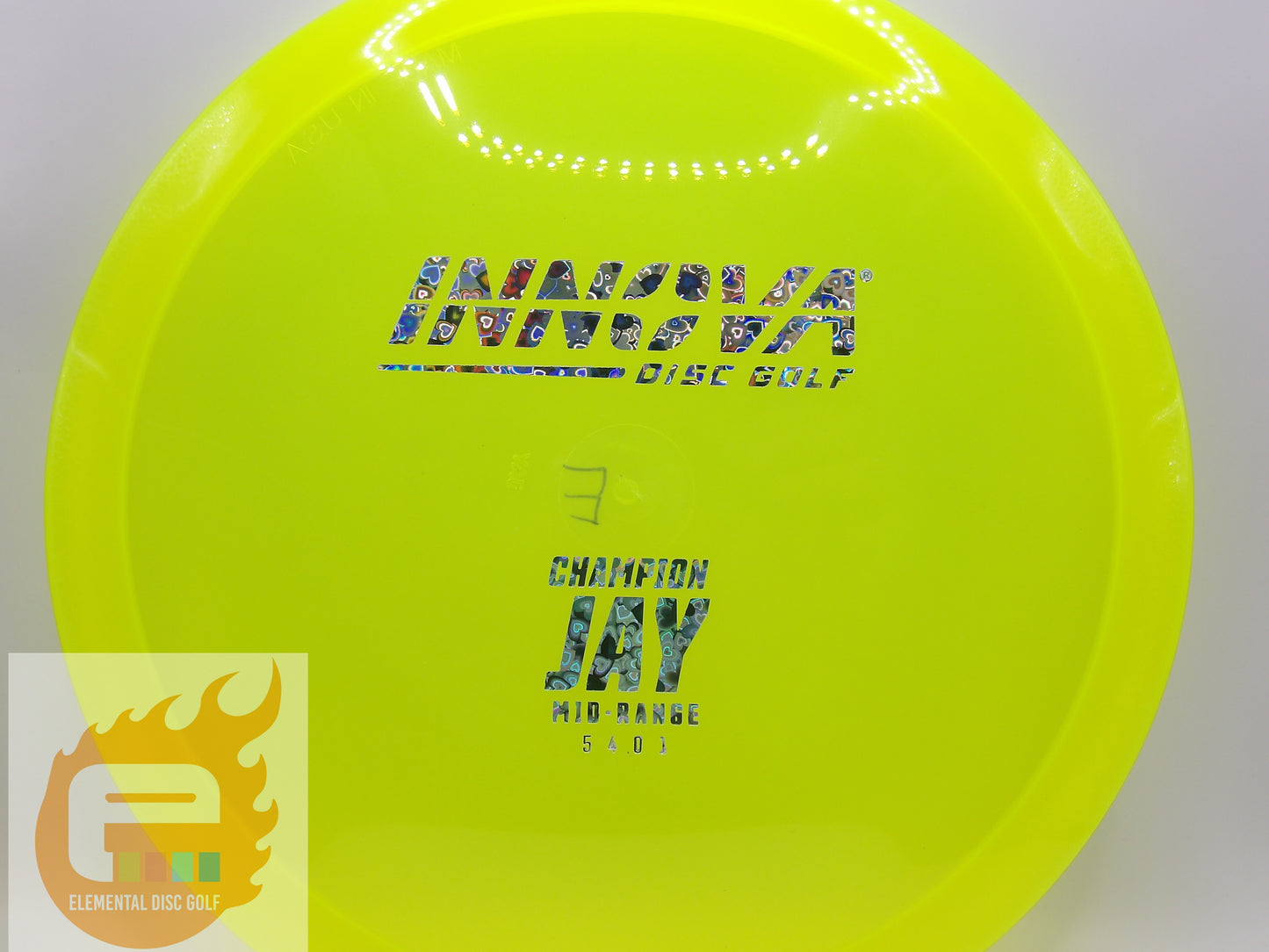 A bright neon yellow-green disc golf disc, specifically the Champion Jay mid-range model by Innova, featuring a holographic foil stamp. The disc is photographed against a neutral light gray background with a white circular ring reflection near the top.